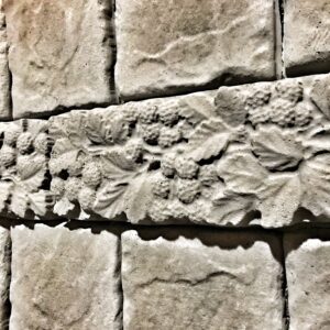 Cast concrete raspberry-pattern decorative strip installed against a stone wall