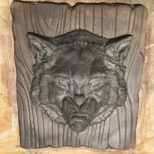 Cast concrete wolf head wall relief on a wood-grain background