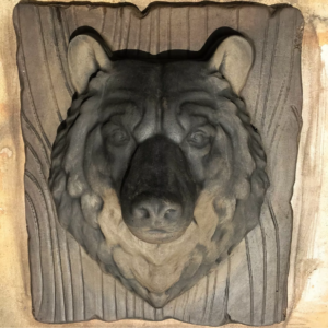 Cast concrete bear head wall relief on a wood-grain plank surround