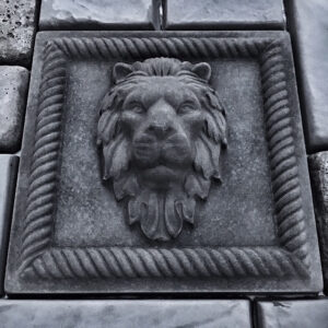 Square cast concrete lion head wall relief installed among stone pavers